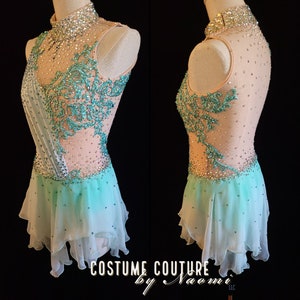 May include: A light pink and turquoise figure skating costume with a high neckline, sleeveless bodice, and a layered tulle skirt. The bodice is embellished with rhinestones and turquoise floral embroidery. The skirt is a gradient of light pink to turquoise. The costume is displayed on a mannequin. The text "COSTUME COUTURE by Naomi LLC" is visible at the bottom of the image.