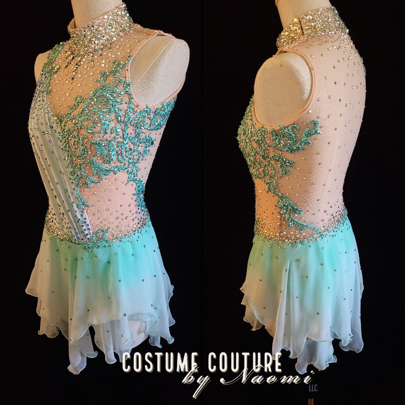 May include: A light pink and turquoise figure skating costume with a high neckline, sleeveless bodice, and a layered tulle skirt. The bodice is embellished with rhinestones and turquoise floral embroidery. The skirt is a gradient of light pink to turquoise. The costume is displayed on a mannequin. The text "COSTUME COUTURE by Naomi LLC" is visible at the bottom of the image.