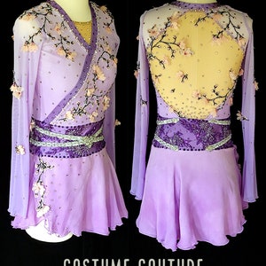 Puede incluir: Un vestido de patinaje art&iacute;stico de color lavanda con mangas largas y un dise&ntilde;o floral. El vestido tiene un cintur&oacute;n morado y plateado y una espalda transparente con un dise&ntilde;o floral. El vestido est&aacute; etiquetado como "Costume Couture by Naomi".
