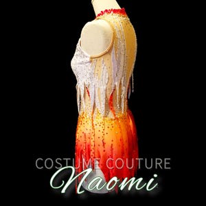 K&ouml;nnte beinhalten: Ein wei&szlig;es und orangefarbenes Trikot mit Flammenmuster. Das Trikot ist mit Strasssteinen verziert und hat einen wei&szlig;en Netz&uuml;berzug. Das Trikot befindet sich auf einer Schaufensterpuppe und der Text "Costume Couture Naomi" befindet sich am unteren Rand des Bildes.