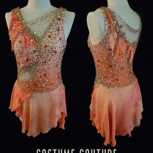 May include: A custom-designed ice skating costume with a peach-colored bodice and skirt. The bodice is embellished with rhinestones and sequins, and the skirt has a layered, ruffled design. The costume is designed by Costume Couture by Naomi.