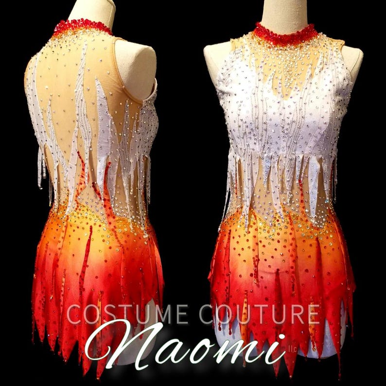 K&ouml;nnte beinhalten: Ein wei&szlig;es und orangefarbenes Eiskunstlaufkost&uuml;m mit Flammenmuster und Strasssteinen. Das Kost&uuml;m hat ein &auml;rmelloses Oberteil und einen Rock mit einem gezackten Saum. Der Text "COSTUME COUTURE Naomi LLC" ist auf dem Rock aufgedruckt.