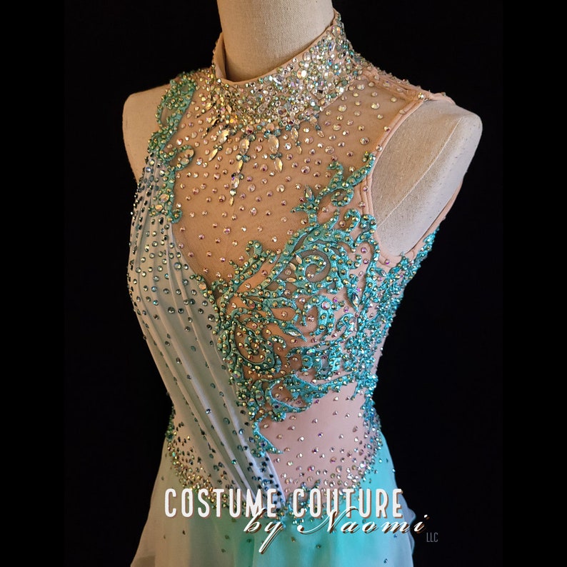 May include: A turquoise and nude sleeveless dance costume with a high neckline and intricate crystal embellishments. The costume features a sheer bodice with a floral design and a flowing skirt. The text "Costume Couture by Naomi LLC" is visible at the bottom of the image.