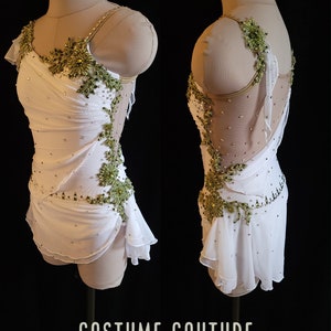 Puede incluir: Traje de patinaje art&iacute;stico blanco con un dise&ntilde;o de adornos verdes y cristales. El traje tiene un corpi&ntilde;o drapeado y una falda con volantes. El texto "COSTUME COUTURE by Naomi" est&aacute; en la parte inferior de la imagen.