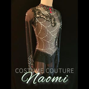 Puede incluir: Vestido de patinaje art&iacute;stico negro con mangas largas y cuello alto. El corpi&ntilde;o presenta un dise&ntilde;o de telara&ntilde;a con adornos blancos y rojos. El texto "COSTUME COUTURE Naomi" se muestra en la parte inferior.