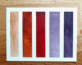 May include: A color swatch card with five vertical stripes of paint. The stripes are beige, orange, red, purple, and dark purple.