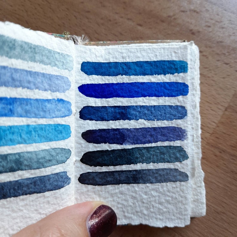 May include: A watercolor swatch book with a variety of blue and indigo shades. The swatches are arranged in rows, with the lightest shades at the top and the darkest shades at the bottom.