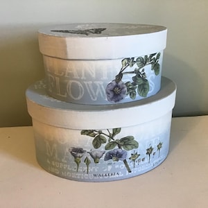 May include: Two round, blue and white storage boxes with floral designs and text that reads "Plant Flowers" and "May Your Garden Be A Suppleant To Your Needs And Horticulture".