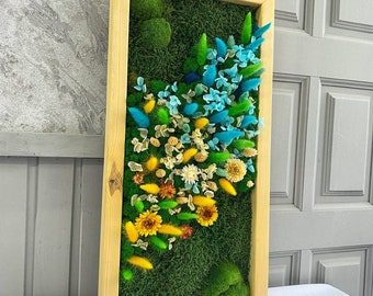 May include: A framed moss wall art piece with a variety of dried flowers in shades of blue, yellow, and green. The flowers are arranged in a cascading pattern, creating a natural and organic look.