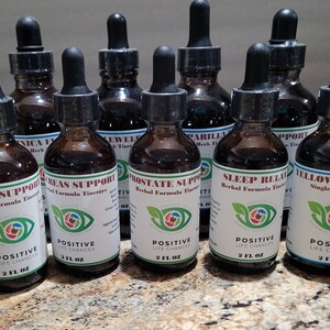 K&ouml;nnte beinhalten: Zehn Glasflaschen mit Tropfern, gef&uuml;llt mit brauner Fl&uuml;ssigkeit. Jede Flasche hat ein wei&szlig;es Etikett mit einem gr&uuml;nen Blattdesign und Text, der "Positive Life Changes" und den Namen einer Kr&auml;uterformel-Tinktur lautet. Die Tinkturen umfassen Liver Support, Breas Support, Prostate Support, Sleep Relax und Yellow Dock.