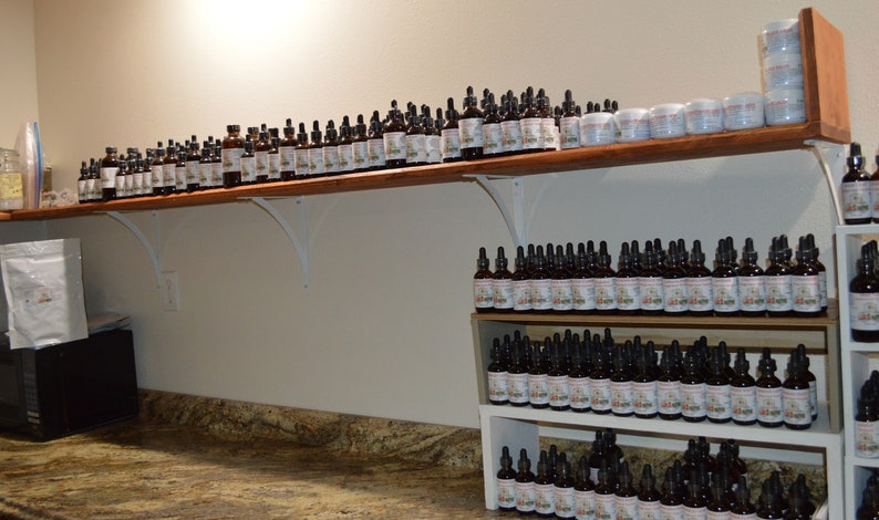 Puede incluir: Un estante lleno de filas de peque&ntilde;as botellas de vidrio marr&oacute;n con goteros. Las botellas est&aacute;n etiquetadas con texto blanco y est&aacute;n dispuestas de forma ordenada y organizada. Las botellas probablemente est&eacute;n llenas de aceites esenciales o tinturas.