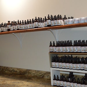 K&ouml;nnte beinhalten: Ein Regal gef&uuml;llt mit Reihen kleiner brauner Glasflaschen mit Tropfern. Die Flaschen sind mit wei&szlig;em Text beschriftet und in einer ordentlichen und organisierten Weise angeordnet. Die Flaschen sind wahrscheinlich mit &auml;therischen &Ouml;len oder Tinkturen gef&uuml;llt.