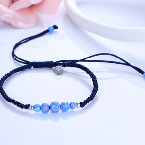 May include: A navy blue braided bracelet with blue and silver beads. The bracelet has a sliding knot closure for adjustable sizing. The beads have a marbled appearance, with shades of blue and white.