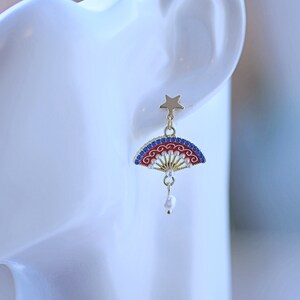 May include: Gold tone earrings with a red, white and blue fan design and a pearl drop. The fan has a gold star at the top.