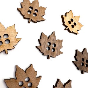 May include: Wooden leaf-shaped buttons in various shades of brown. Each button has four holes for sewing. The buttons are arranged on a white background, creating a natural and rustic aesthetic. Ideal for fall-themed crafts and sewing projects.