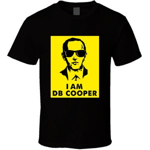 May include: Black t-shirt with a yellow rectangle featuring a black and white silhouette of a man wearing sunglasses and the text "I AM DB COOPER".