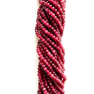 May include: A strand of deep red faceted gemstone beads. The beads are small and round, and they are strung together on a clear thread.