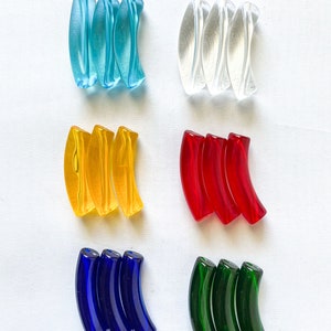 May include: An assortment of colorful, curved glass beads in various shades. The colors include light blue, clear, yellow, red, dark blue, and green. Each set contains three beads, arranged in a row. The beads have a smooth, glossy finish.