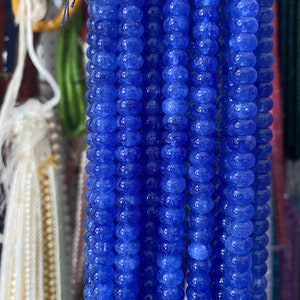May include: A close-up of multiple strands of blue gemstone beads. The beads are round and have a slightly textured surface.