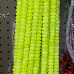 May include: A strand of bright yellow beads, likely made of jade or glass, with a smooth, rounded shape. The beads are strung together on a thin thread and are arranged in a vertical line.