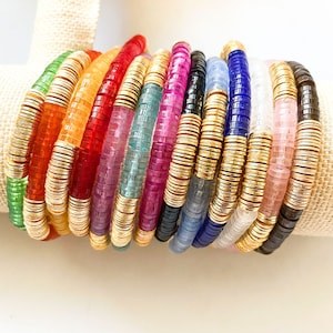 May include: A stack of colorful beaded bracelets with gold accents. Each bracelet features a different color of beads, including red, blue, green, pink, and purple.