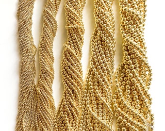 May include: Five strands of gold-colored beads, each with a different texture and size. The beads are arranged vertically and are all the same color.