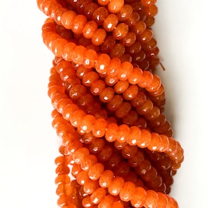 May include: A strand of orange faceted gemstone beads. The beads are round and have a smooth, polished finish.