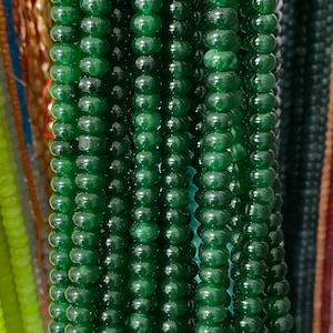 May include: A strand of dark green glass beads, each bead is round and smooth. The beads are strung together on a clear thread.