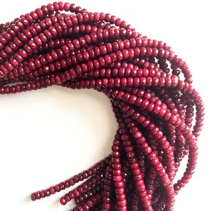 May include: A strand of deep red faceted gemstone beads. The beads are small and round, and they are strung together on a clear thread. The beads are arranged in a loose coil.