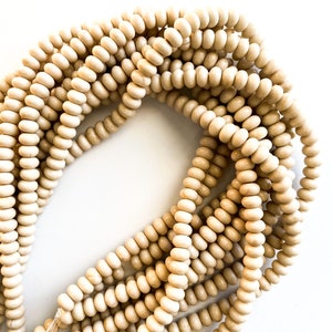 May include: A strand of natural wood beads in a creamy off-white color. The beads are round and smooth, and they are strung together on a clear thread.