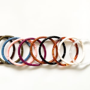 May include: Ten colorful bracelets made of stacked plastic beads. The bracelets are in various colors, including brown, green, pink, purple, blue, black, orange, white, and clear.