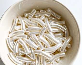 May include: A bowl filled with white, curved plastic beads. The beads are smooth and shiny, and they are arranged in a random pattern.