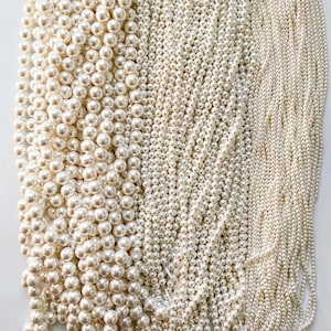 May include: A collection of white pearl beads in various sizes and shapes. The beads are arranged in rows, creating a visually appealing pattern.