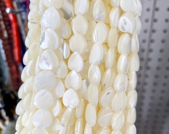 May include: A strand of white mother of pearl heart shaped beads. The beads have a slight iridescent sheen.