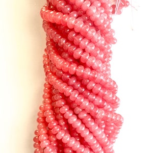 May include: A strand of pink gemstone beads. The beads are round and have a smooth, polished finish. The beads are strung on a clear thread.