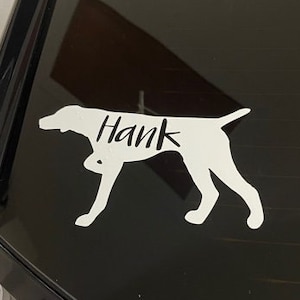 May include: A white vinyl decal of a dog silhouette with the name "Hank" on the back of a black car.