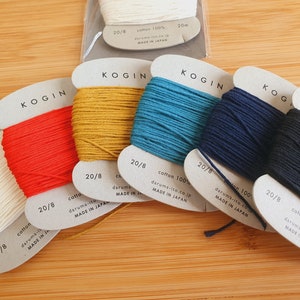 Puede incluir: Seis carretes de hilo de bordar de algodón 20/8 en varios colores, incluyendo blanco, rojo, amarillo, azul verdoso, azul marino y negro. Cada carrete está etiquetado con "KOGIN" e incluye el texto "cotton 100% daruma-ito.co.jp MADE IN JAPAN".