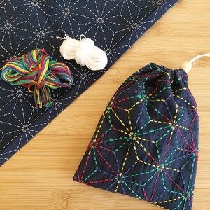 Puede incluir: Una bolsa de tela azul oscuro con un patr&oacute;n geom&eacute;trico de estrellas multicolor, cierre de cord&oacute;n con una cuenta de madera, una pieza de tela azul oscuro a juego con costuras de estrellas blancas, hilo de bordar arco&iacute;ris e hilo blanco.