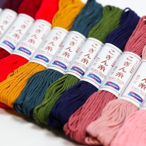 May include: A collection of ten spools of colourful embroidery floss, each labelled with Japanese text and the words "Kogin Thread Cotton 100%". The colours include red, orange, yellow, green, blue, pink, and light pink.