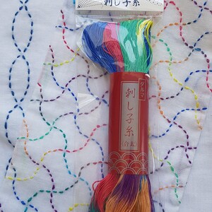 Puede incluir: Una madeja de hilo de bordar multicolor en un paquete de pl&aacute;stico transparente con una etiqueta de papel roja que presenta texto en japon&eacute;s. El hilo muestra un degradado de tonos azules, verdes, amarillos, rosas y morados. El encabezado tambi&eacute;n tiene texto.