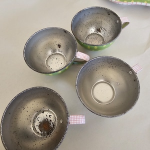 May include: Four vintage metal teacups with green and white polka dot designs and pink and white checkered handles. The cups are slightly worn and have a rustic look.