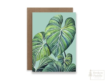 May include: A greeting card featuring a watercolor illustration of green tropical leaves on a light blue background.