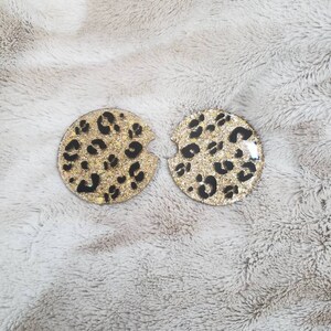 May include: Two round coasters with a gold glitter and black leopard print design.