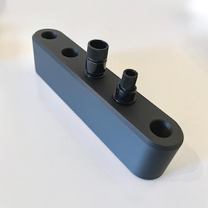 May include: A black rectangular object with three cylindrical holes and two black knobs. The object has rounded edges and a matte finish, suggesting a modern design. The knobs have a ridged texture.