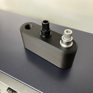 May include: A black, rectangular object with two metal posts. One post is black, and the other is silver. The object has a hole on one end. The surface has a textured, layered appearance.