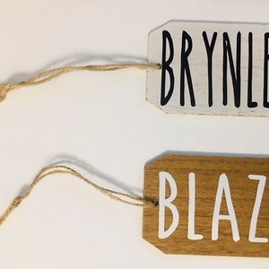 May include: Two wooden gift tags with twine. The top tag is white with black lettering that reads "BRYNLEE". The bottom tag is brown with white lettering that reads "BLAZE".