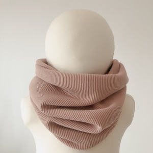 Könnte beinhalten: Ein weicher, gerippter, staubiger rosafarbener Halsschmeichler. Der Halsschmeichler ist aus einem dehnbaren Stoff gefertigt und perfekt, um sich im Winter warm zu halten.