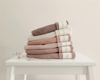 May include: A stack of six folded ribbed beanies in shades of mauve, cream, and dusty rose. Each beanie is secured with a white paper band featuring the printed text Hej, cool, love, ohdabaum, and little one in black ink.