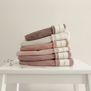 Könnte beinhalten: Ein Stapel aus sechs gerippten Stoffleggings in verschiedenen Rosétönen und Beige. Die Leggings sind gefaltet und auf einem weißen Tisch gestapelt. Jede Leggings hat ein Etikett mit dem Text "Hej. cool. love. vendac. ABAU. little."