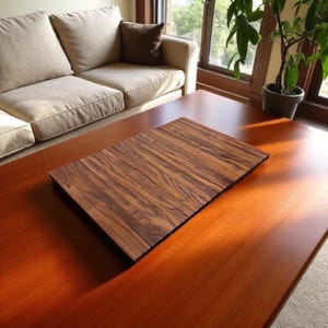 Könnte beinhalten: Ein rechteckiges Serviertablett aus Holz mit einem dunkelbraunen, gestreiften Muster liegt auf einem größeren, rotbraunen Couchtisch aus Holz. Die Oberfläche des Tabletts besteht aus einzelnen Holzbrettern. Der Couchtisch befindet sich in einem Wohnzimmer.